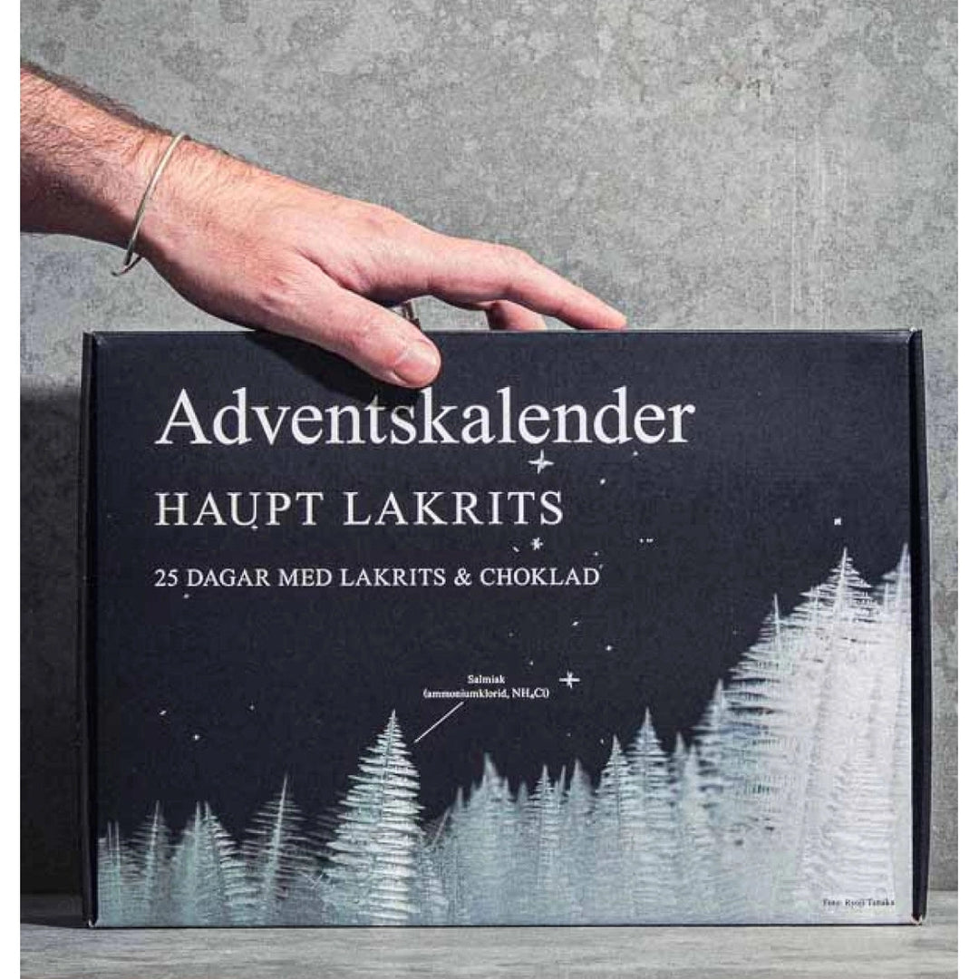 Haupt Lakritsi Adventskalenteri 2026 kädessä harmaata seinää vasten