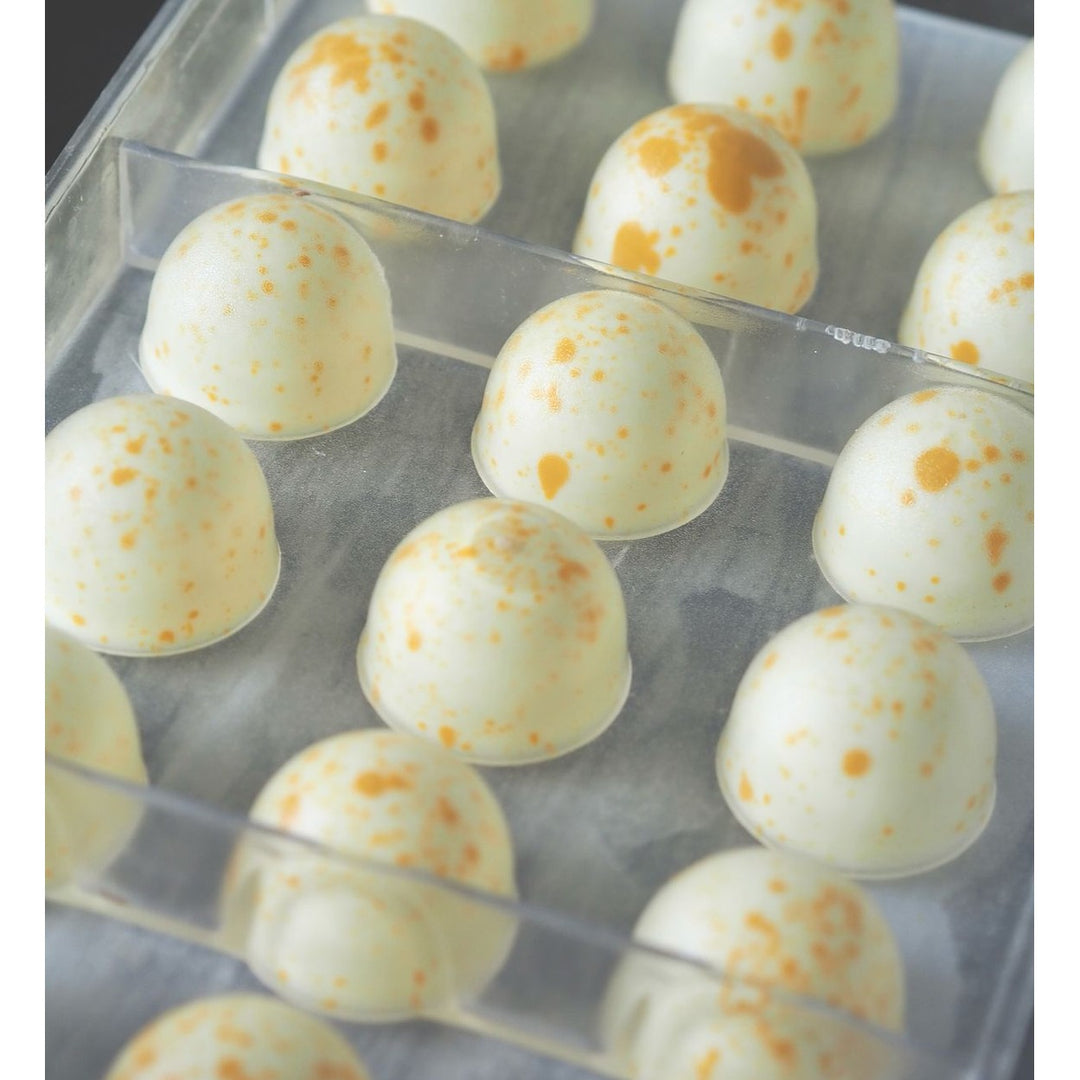 Närbild på vita Callebaut W2 chokladpraliner med orange fläckar i plastform