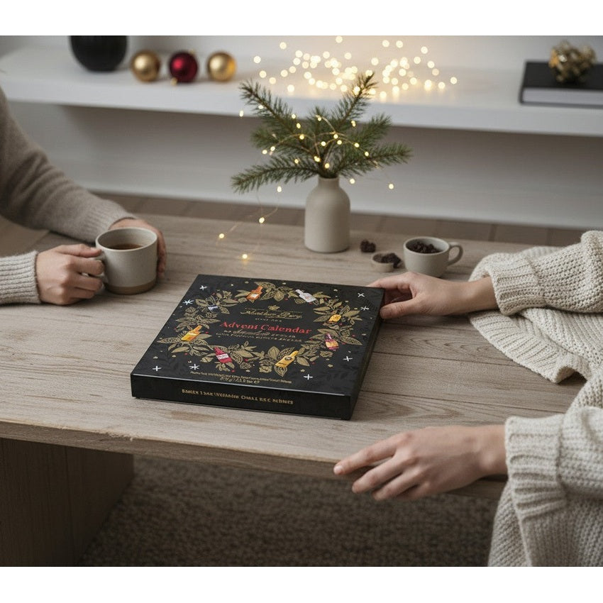 Chokladshopen Anthon Berg likörkalender med julmotiv på ett träbord omgiven av två personer med kaffekoppar